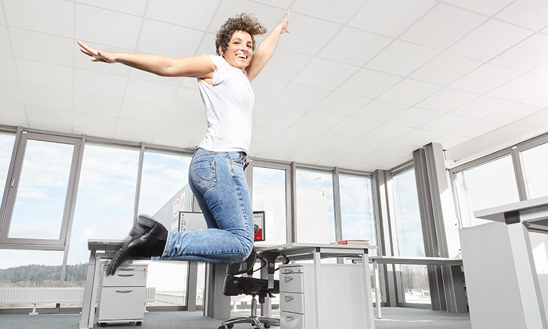 Freude am Arbeitsplatz: Frau springt in Büro nach oben